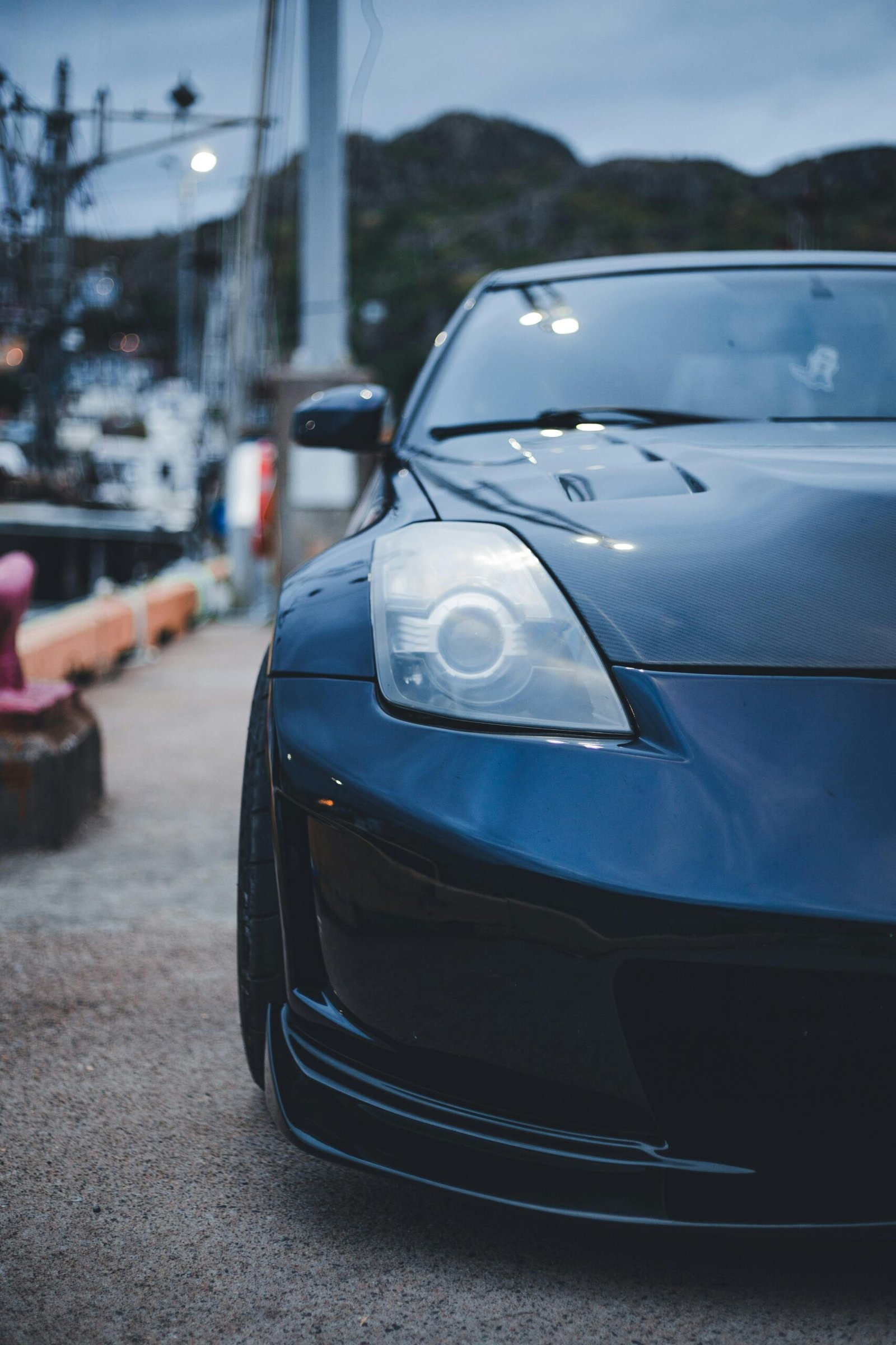 A sleek black sports car is parked on a harbor pathway, showcasing its stylish design.